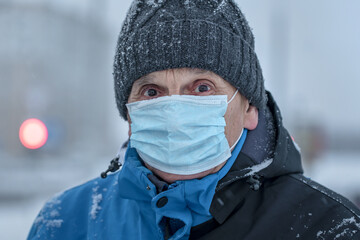 Fototapeta na wymiar Mature sick man in knitted cap and medical face mask at city street