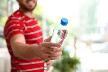 Young man with bottle of water at home, closeup
