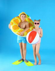 Cute little children in beachwear with inflatable toys on light blue background