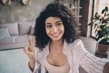 Photo portrait of woman showing v-sign taking selfie talking on video call indoors