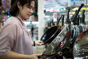 Female housewife or cook choosing teflon frying pan or deciding to buy steel frying pan for cooking in her kitchen,asian woman comparing two products,shopping for new pan in household goods department