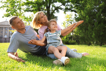 Naklejka na ściany i meble Happy parents with their child having fun on green grass. Spending time in nature