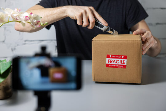 man recording unboxing video with mobile phone. cutting cardboard box with knife. social media marketing