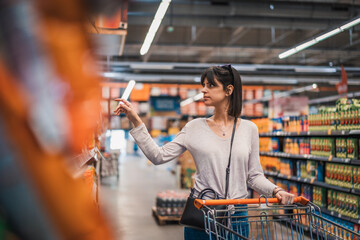 Sale, shopping, consumerism and people concept. Woman in supermarket with shopping trolley choosing...