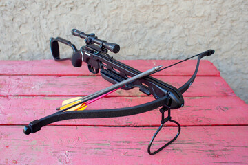 A modern crossbow with arrows and an optical sight lies on a wooden table in the street