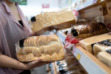 Wall murals Bread Hands of girl holding sliced white bread product,choosing wheat bread in plastic bag packaged,fresh homemade baked bread in the bakery shop while shopping food,woman buying or selecting food quality
