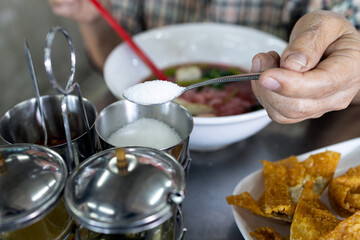Hand of senior woman holding spoon full of white cane sugar,old elderly eat food that tastes sweet,people scooping sugar from condiment into her bowl of noodles,seasoning,flavoring food with sugar