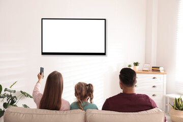 Family watching TV on sofa at home, back view