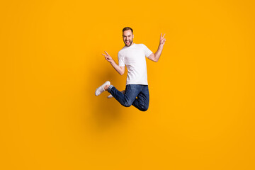 Fototapeta na wymiar Full length body size photo of jumping cheerful male model showing peace sign with two fingers isolated vivid yellow color background