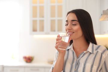 Young woman drinking pure water from glass in kitchen. Space for text
