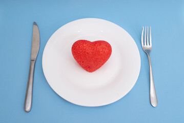 Obraz na płótnie Canvas Red heart on a white plate and cutlery on a blue background