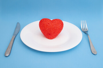 Fototapeta na wymiar Red heart on a white plate and cutlery on a blue background