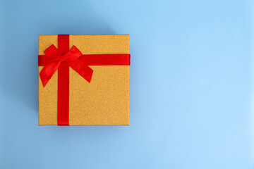 Golden gift box with red ribbon on blue background