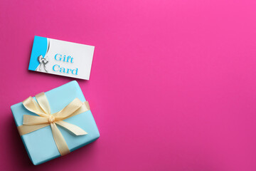 Gift card and present on pink background, flat lay. Space for text