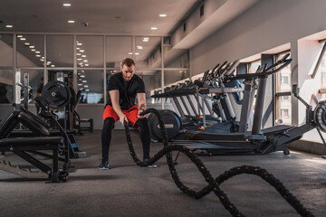 Fototapeta na wymiar Handsome fit man using battle ropes in gym working out