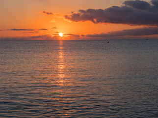 Obraz premium Sunrise with the red orange sun raising up from the sea with dark clouds at beach Spiaggia di Santa Maria Navarrese, Sardinia, Italy