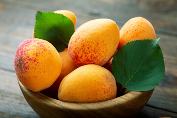 Ripe apricot with leaves in a bowl on a wooden table. Home harvest from your own garden.