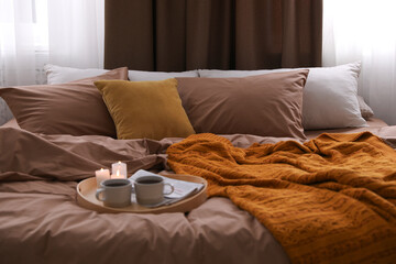 Fototapeta na wymiar Cups of hot drink and candles on bed with brown linens in room