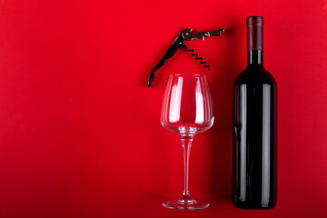 Bottle of red wine and an empty wine glass with a corkscrew next to it. Composition on a red background. Romantic mood. Space for text.