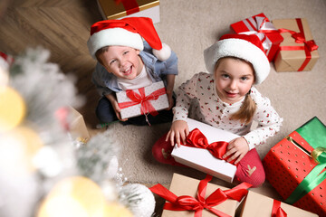 Cute little children with Christmas gifts on floor at home, above view