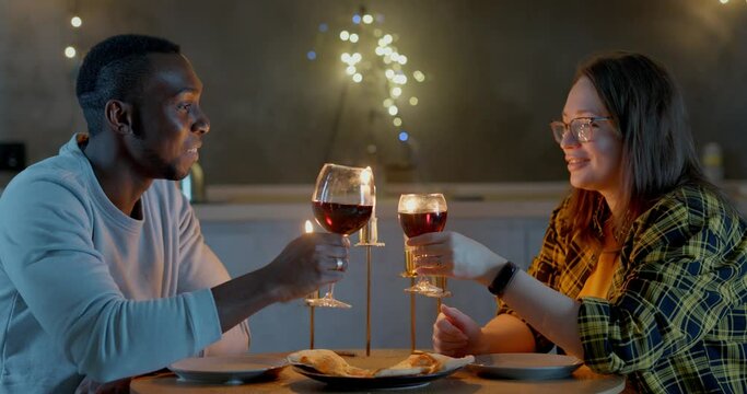 Happy couple celebrating valentine's day. They drink wine in glasses and eat pizza by candlelight.