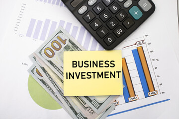 business investment is written on a yellow sheet that lies on dollars with documents near the calculator. Business and financial concept