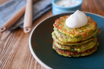 Vegetarian food. Zucchini fritters, thin pancakes and sauce on white plate over wooden table. Squash pancakes