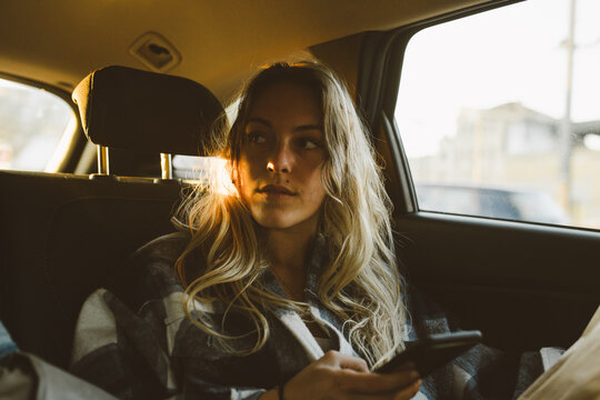 young caucasian female in backseat of car with smartphone