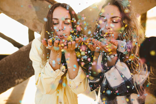two young adult female friends celebrating and having fun blowing confetti