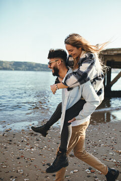happy young adult couple doing piggyback at the beach