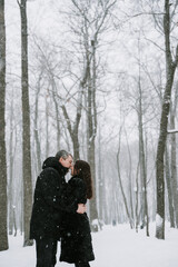 Fototapeta na wymiar A man and a woman on the background of a snow-covered forest in a snowfall