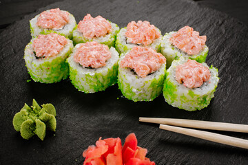 Green sushi rolls with salmon sauce on black background