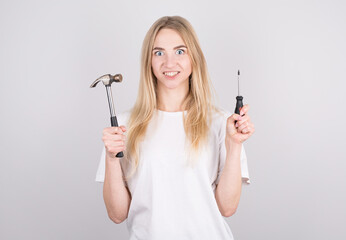The girl holds a hammer and a screwdriver and looks scared, not understanding what to do with it...