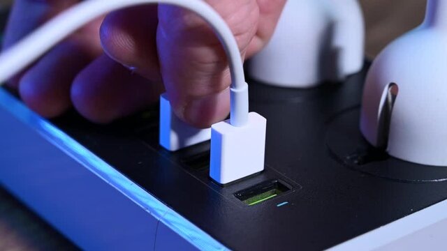 Close-up macro of a male hand unplugging cables from the power outlet. Modern convenient multi-port usb charger for devices. 
