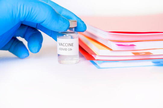 gloved hand holds covid 19 vaccine next to notebooks on white background