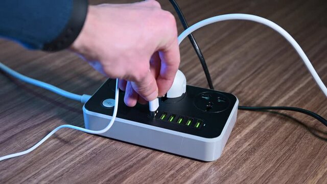 Modern convenient multi-port usb charger for devices. Male hand plugging cables into a power outlet. 