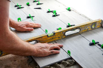 Workers are using plastic clamps and wedges to leveling the large ceramic tile on the floor.