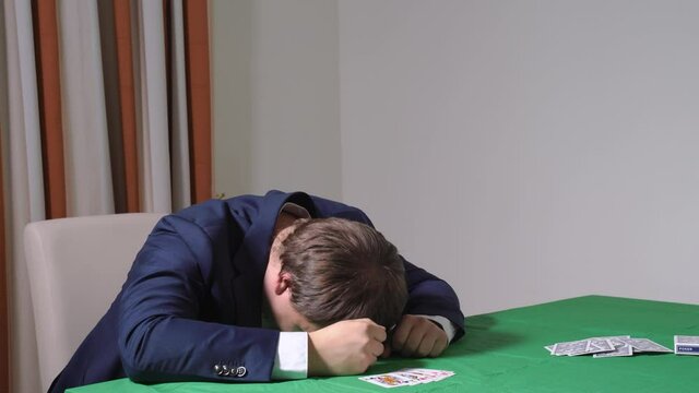 Young businessman in suit had lost last money savings in poker game, so he put head down on table in despair. Problems with psychological addictions of person.
