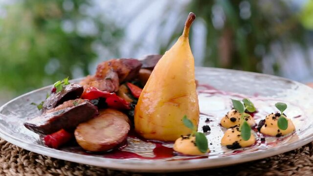 Close up view on spinning plate served sliced duck breast magret served with barbecue vegetables, sauce and pear. Restaurant dish food concept