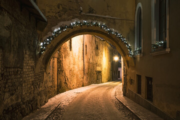 Obraz premium Beautiful narrow street of Vilnius Old Town, evening or night view with old buildings and street lamp in winter with snow