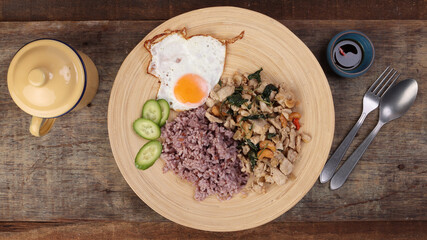 Thai fusion stair fried chicken with Thai basil and cashew nut with health brown rice fried egg sauce cucumber on woody plate over rustic wood background fork spoon
