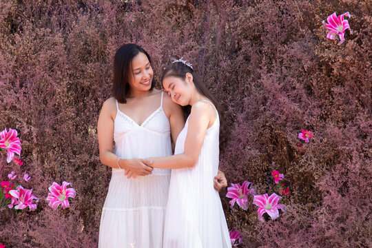 Beautiful Asian couple with with lace wedding LGBT women spent time together in park, Attractive 2 women hold hand in hand hug with love in garden background, Valentine's Day Concept