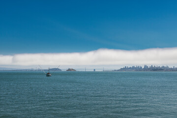 View of the San Francisco Bay with a fishing trawler, the Oakland Bay Bridge, the Alcatraz Island and the city of San Francisco skyline on the background.