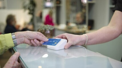 Close Up Of Senior Woman Making Contactless Payment To Stylist In Salon With Credit Card