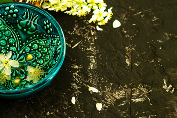 A blue oriental Turkish bowl with transparent water on a background of white cherry flowers on a wooden board and a black background. Copy space. Spring holiday concept