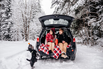 couple guy and girl sitting in car playing with dog in winter forest