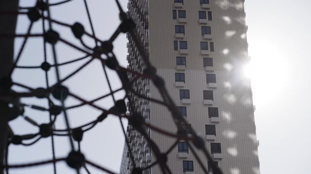 Details of outdoors modern children playground with different sports equipment. Action. Close up of climbing net for children on the background of residential high rise building and blue sky.