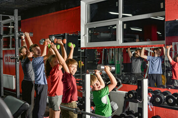 A sportive family with children in the gym is engaged with dumbbells.