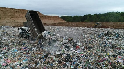 Aerial view. A dump truck unloads a pile of garbage at a landfill. Dump of unsorted waste. Drone shot of working trash management. - Powered by Adobe
