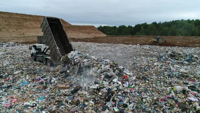 Aerial view. A dump truck unloads a pile of garbage at a landfill. Dump of unsorted waste. Drone shot of working trash management.